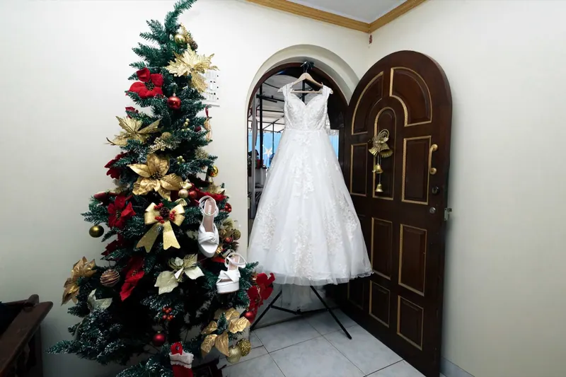 White wedding gown hanging in an arched doorway beside a Christmas tree at the bride's home