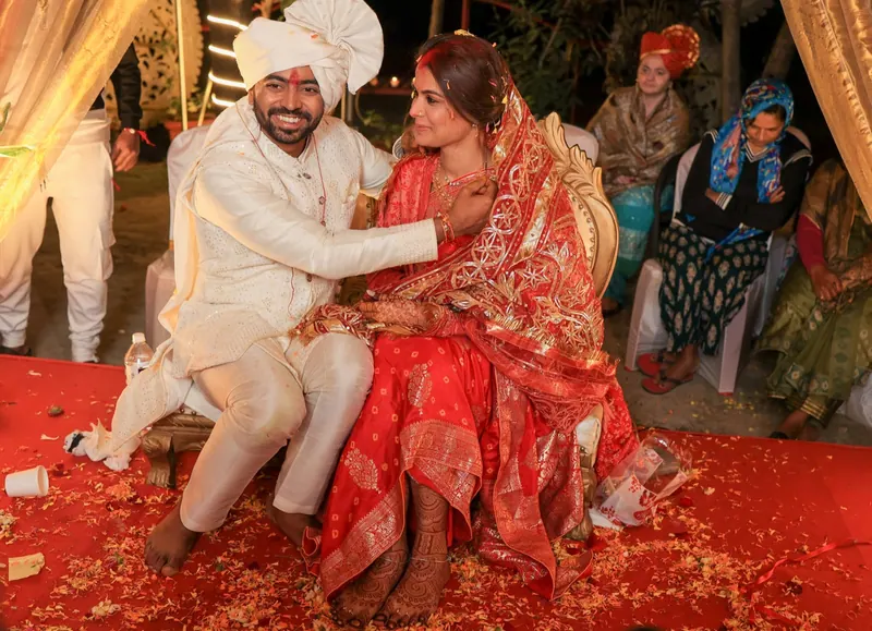 Groom and bride seated on the mandap, petals scattered on a red carpet