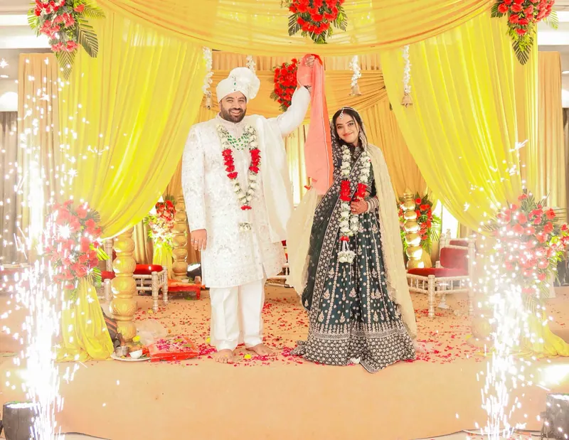Couple raise joined hands on a yellow-draped stage as cold sparklers fire on both sides